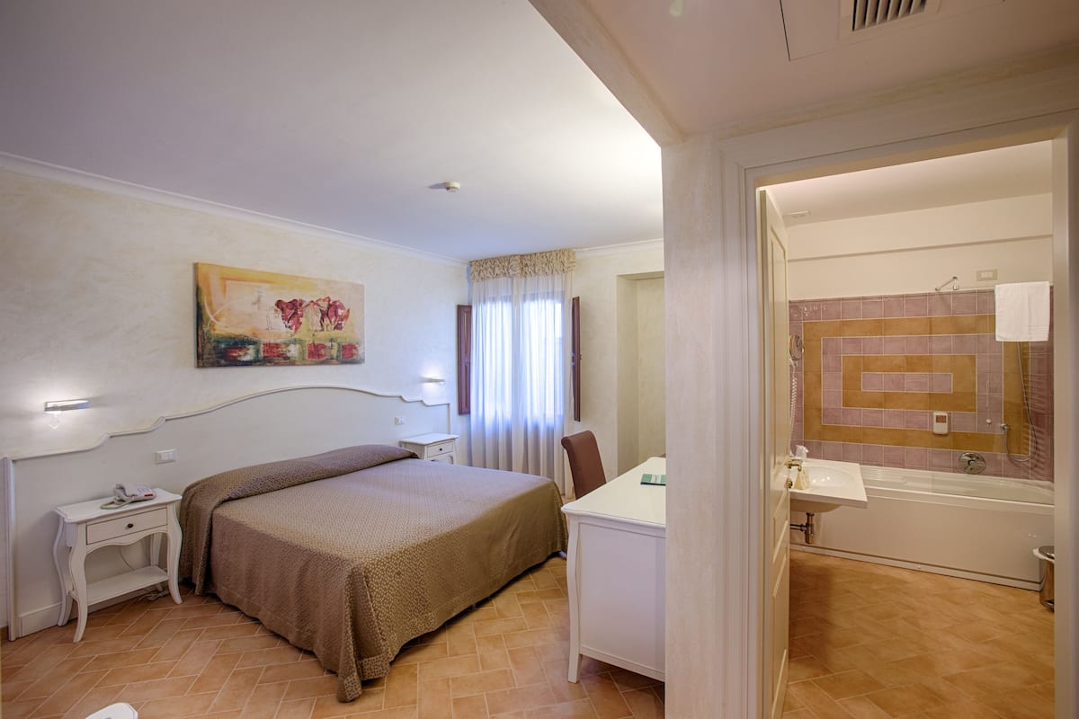 A hotel room with a bed, bedside table, desk, and a bathroom with a bathtub and sink.