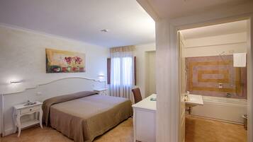 A hotel room with a bed, bedside table, desk, and a bathroom with a bathtub and sink.