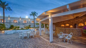 Un patio al aire libre con piso de piedra, mobiliario blanco y una pared de piedra con iluminación empotrada.