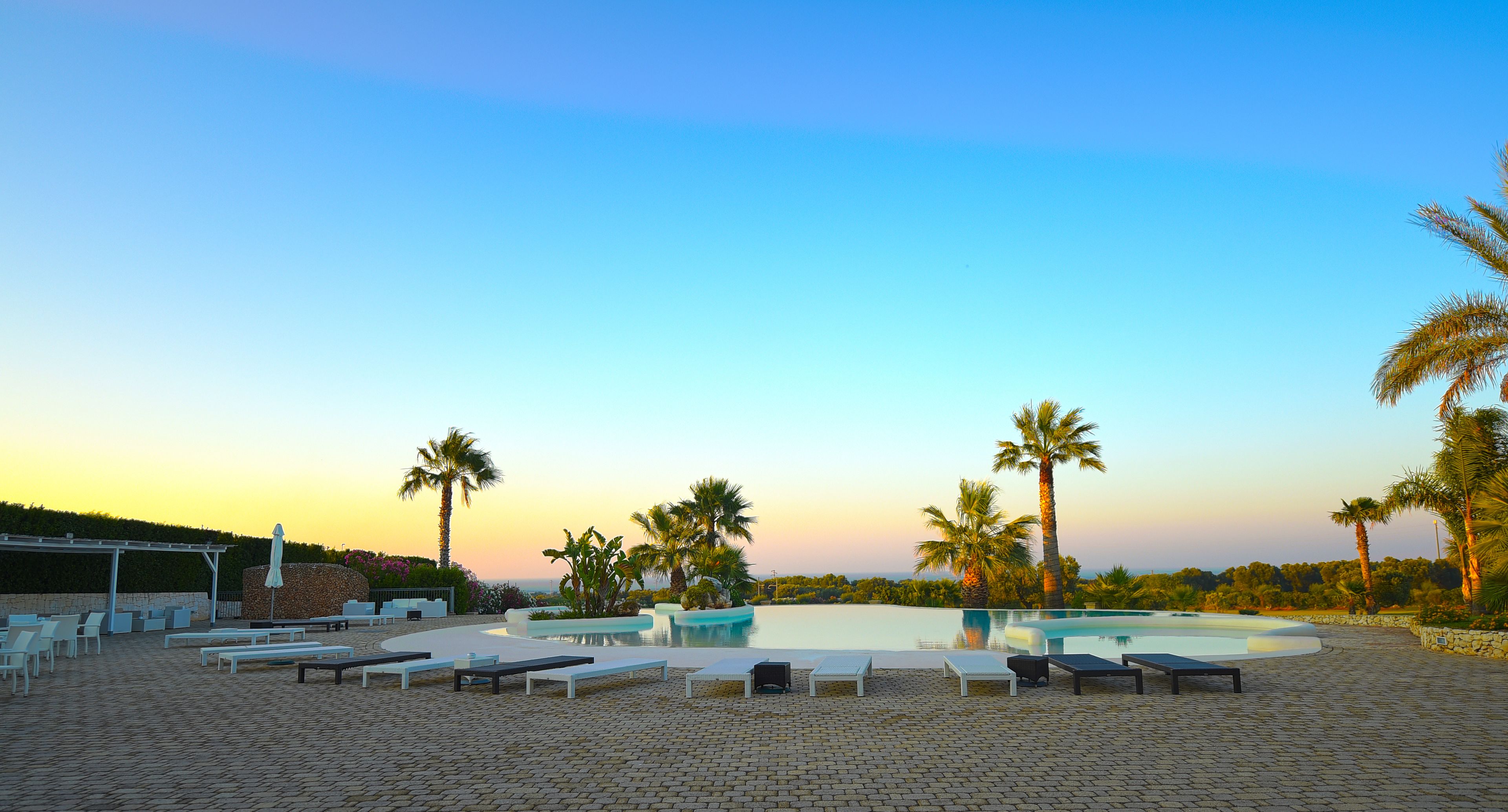 A pool area with lounge chairs and palm trees.