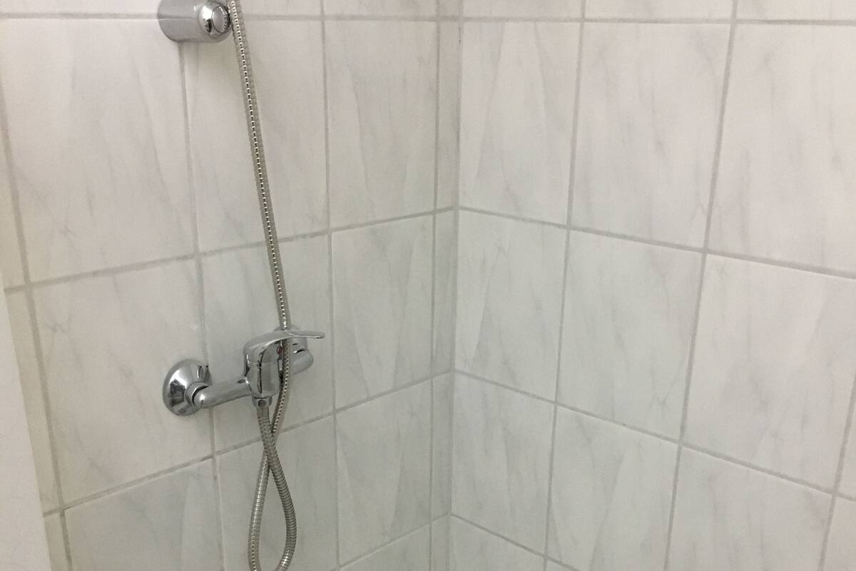 A corner shower with a handheld showerhead, a wall-mounted faucet, and a small shelf above the shower.