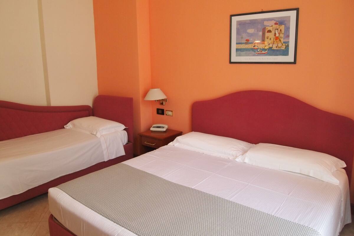 Habitación de hotel con dos camas, una mesita de noche, una lámpara y un cuadro en la pared.