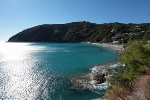 Vista costera con un mar turquesa transparente, costa rocosa y una ladera con edificios.