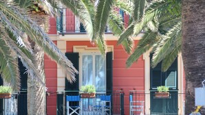Un edificio de fachada roja, balcones con plantas en macetas y una palmera en primer plano.