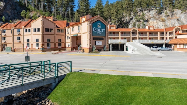 A Quality Inn with a red-roofed building, a parking lot, and a green fence. - Quality Inn Keystone near Mount Rushmore (Keystone)