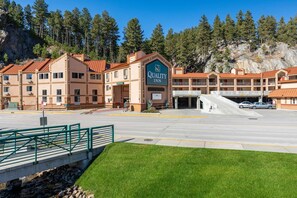 A Quality Inn with a red-roofed building, a parking lot, and a green fence. - Quality Inn Keystone near Mount Rushmore (Keystone)