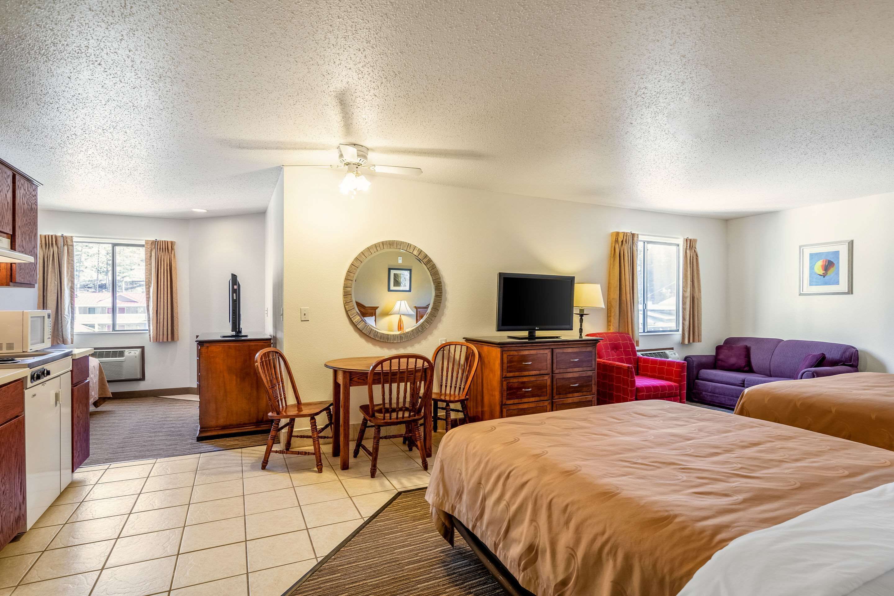 A hotel room with a bed, a desk with a chair, a television, a couch, and a small kitchen area.