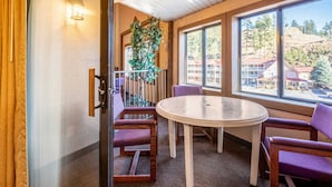 A room with a round table and four purple chairs, a potted plant, and a view of buildings through large windows. - Quality Inn Keystone near Mount Rushmore (Keystone)