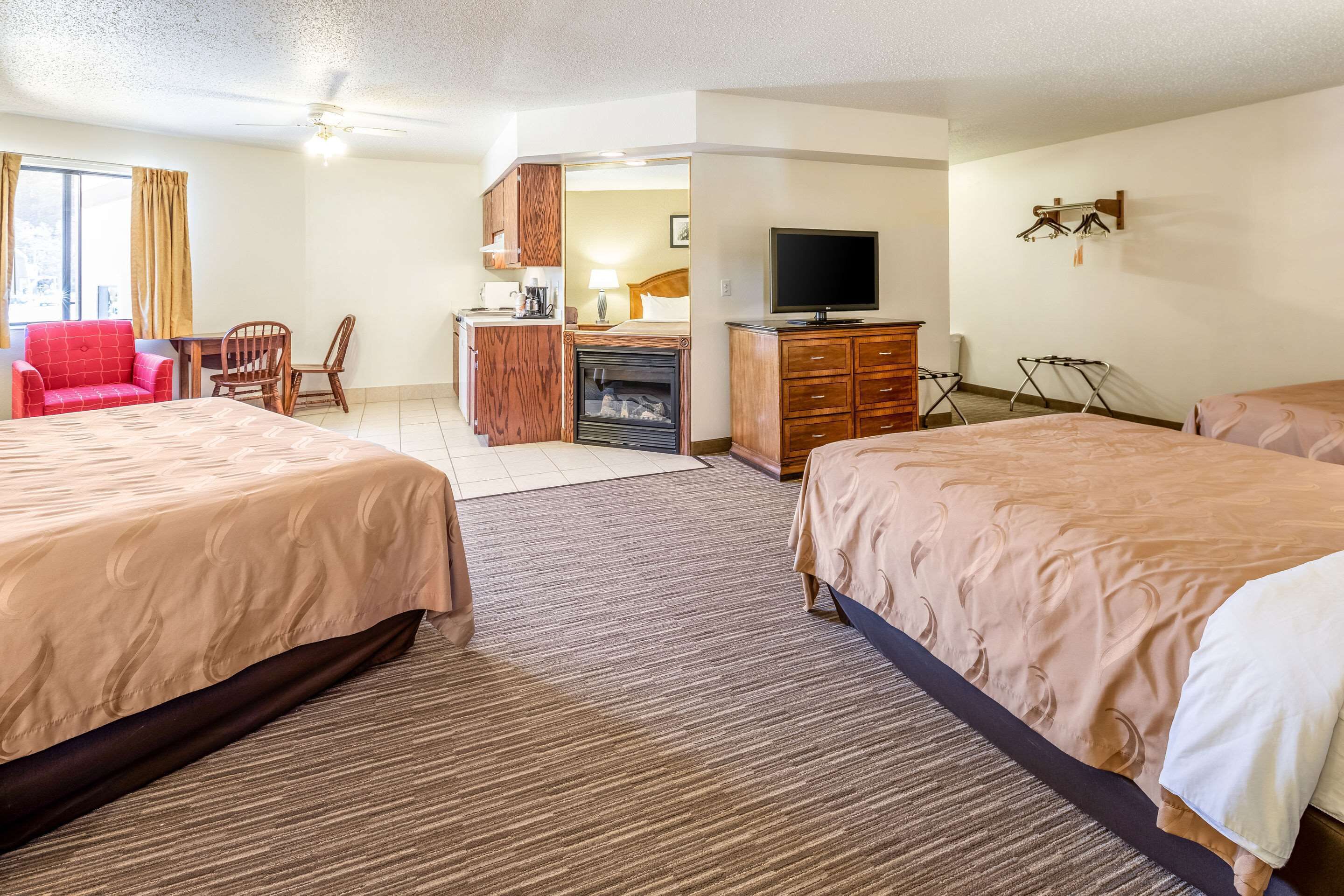 A hotel room with two beds, a desk with a television, a fireplace, and a red chair.