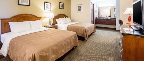 A hotel room with two beds, a TV, a desk, and a bathroom visible through an open door.