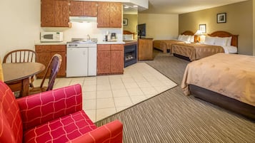 Habitación de hotel con kitchenette, dos camas, un sofá rojo y una pequeña mesa de comedor.