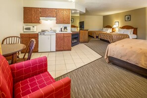 A hotel room with a kitchenette, two beds, a red sofa, and a small dining table.