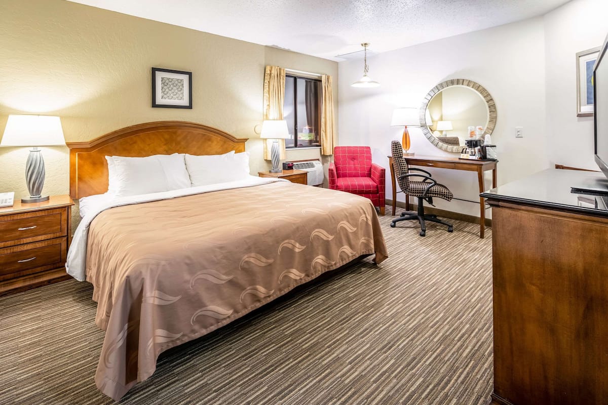 A hotel room with a bed, desk, chair, and a large mirror.