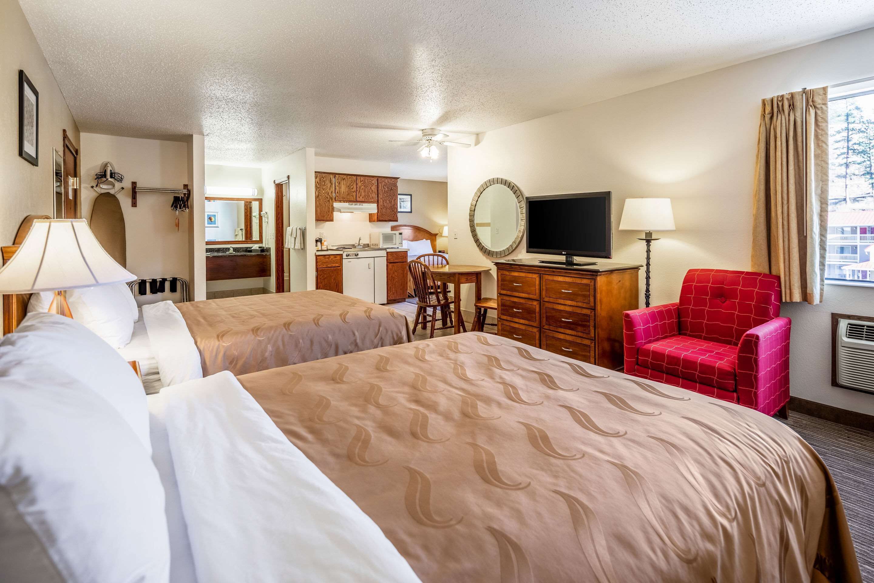 A hotel room with two beds, a desk, a chair, a TV, and a view of the city.