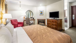 A hotel room with a large bed, a red armchair, a desk with a mirror, a television, and a fireplace. - Quality Inn Keystone near Mount Rushmore (Keystone)