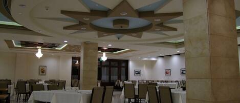 Un comedor amplio con varias mesas y sillas, techo decorativo y suelo pulido.