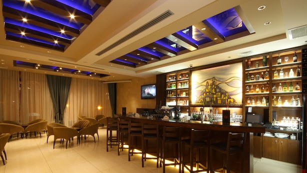 A bar area with a long counter, multiple bar stools, and a television screen. - Manger Square Hotel (Bethlehem)
