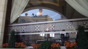 A view through a window with a decorative frame, a patterned wall, and a balcony with orange flowers. - Manger Square Hotel (Bethlehem)