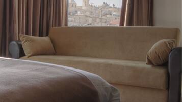 Habitación de hotel con cama, sofá y vista a un paisaje urbano a través de una ventana.