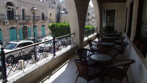 A balcony with wicker chairs and tables, overlooking a street with parked cars and buildings. - Manger Square Hotel (Bethlehem)