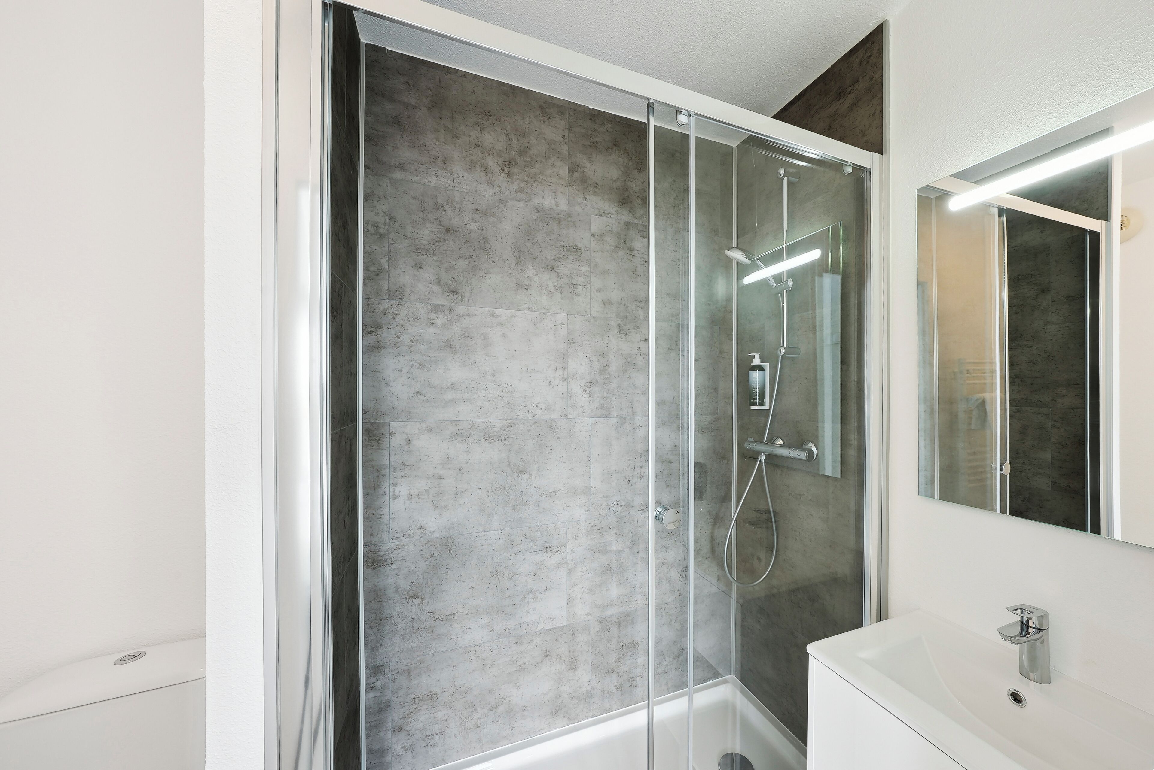 Une salle de bain moderne avec une douche à parois de verre, un lavabo blanc et un grand miroir.
