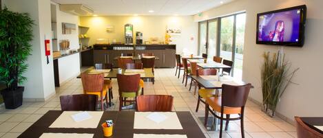 A restaurant with multiple tables, chairs, a kitchen area, and a TV screen.