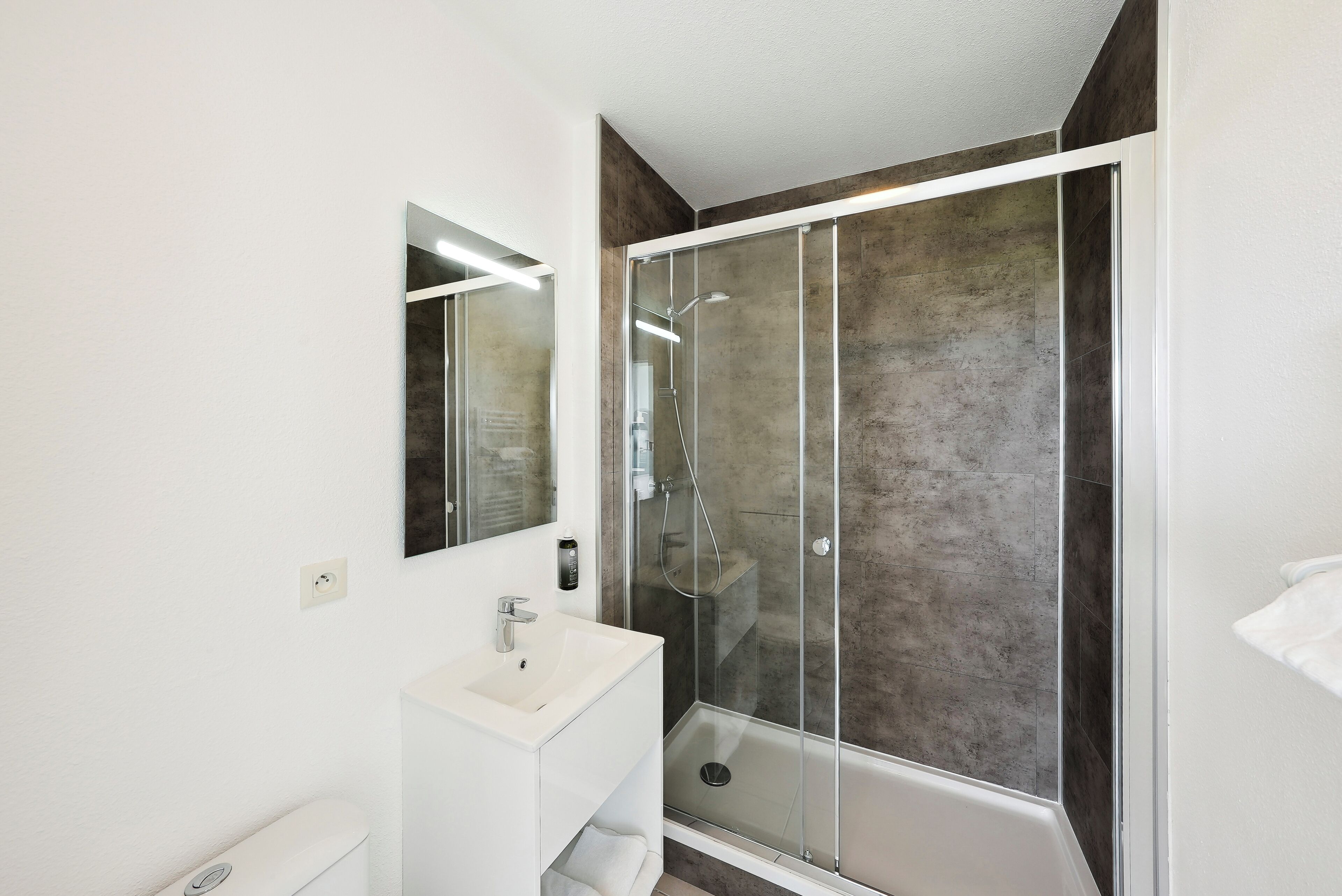 A modern bathroom with a glass-enclosed shower, a white sink, and a large mirror.