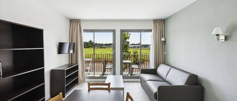 Ein modernes Wohnzimmer mit einer Couch, einem Fernseher, einem Esstisch mit Stühlen und einem Balkon mit Blick ins Freie.