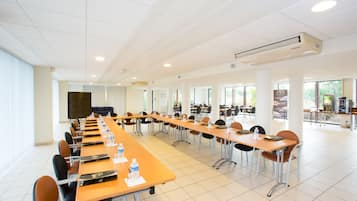 Une grande salle de conférence avec de longues tables et des chaises, un appareil de climatisation et de grandes fenêtres.