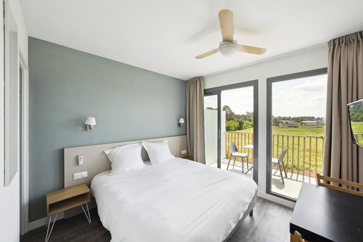 A bedroom with a bed, bedside tables, a ceiling fan, and a view of the outdoors.