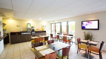 A dining area with multiple tables and chairs, a kitchen area with a refrigerator, and a television mounted on the wall.