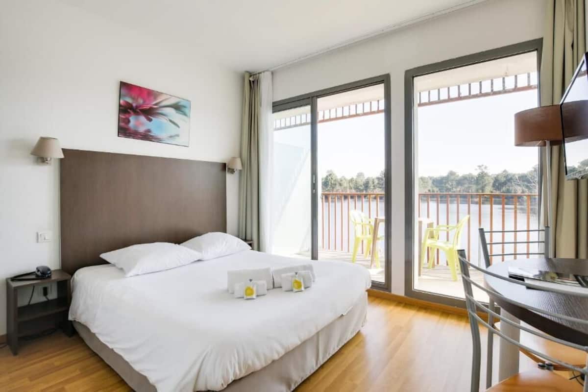 A hotel room with a bed, bedside table, lamp, and a view of the outside balcony.
