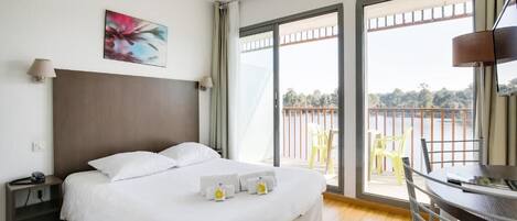A hotel room with a bed, bedside table, lamp, and a view of the outside balcony.