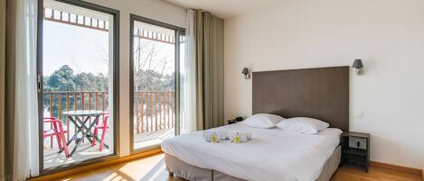 A hotel room with a large bed, a nightstand, and a view of a balcony with chairs and a table.