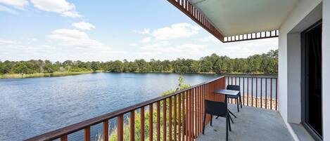 A balcony with a view of a lake, a table, and chairs.