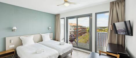 A hotel room with two beds, a desk, a TV, and a balcony with a view.