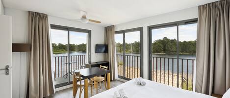 A hotel room with a bed, a desk, a chair, a television, and a balcony with a view of a lake.