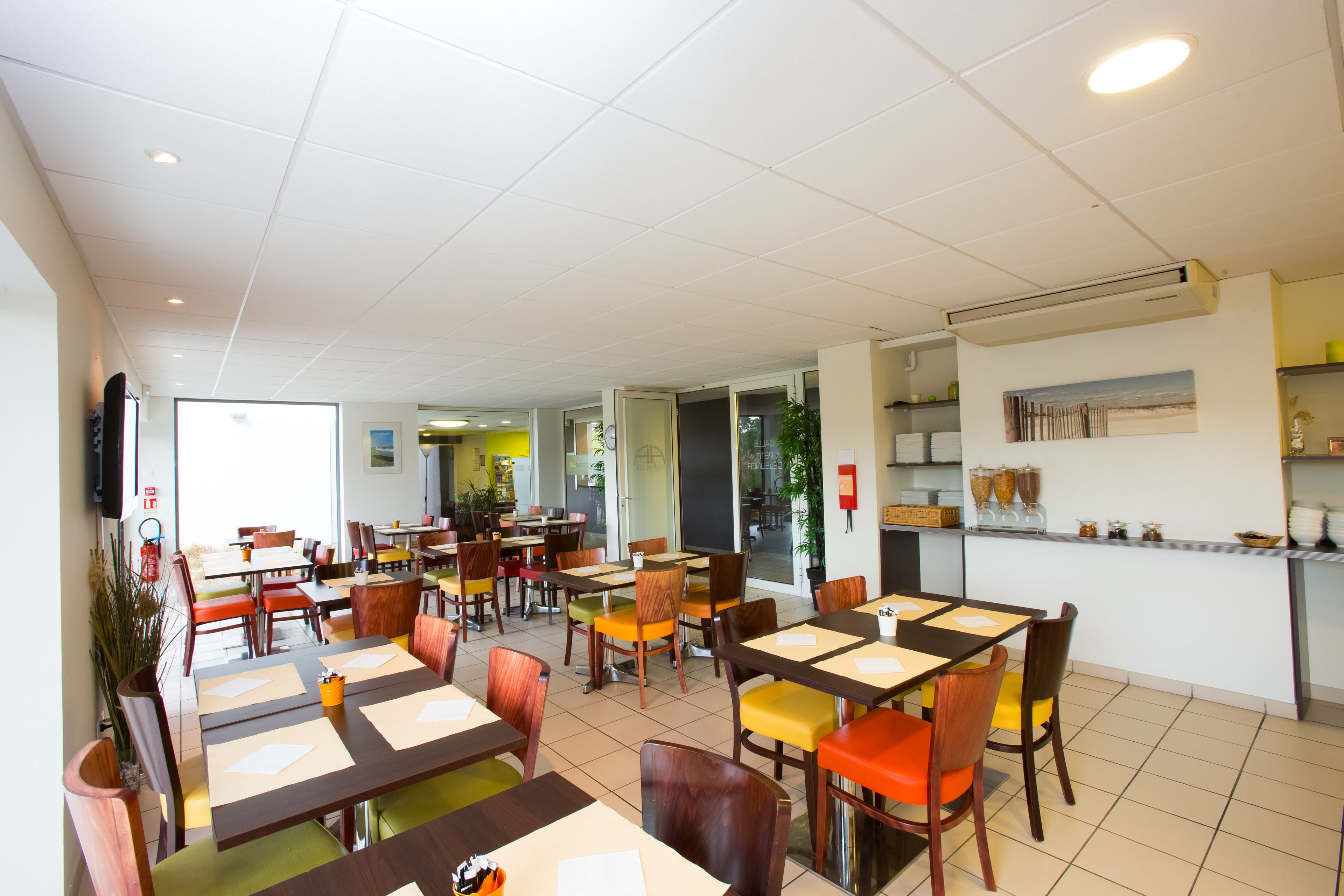 Un grand espace dédié à la salle à manger, avec plusieurs tables et chaises, un coin cuisine et une vue sur l’extérieur.