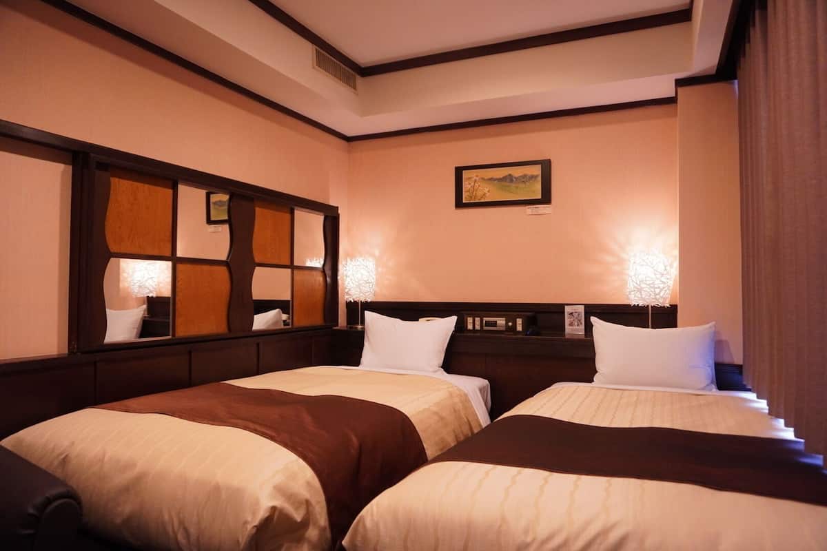 Habitación de hotel con dos camas, un espejo grande y un cuadro en la pared.