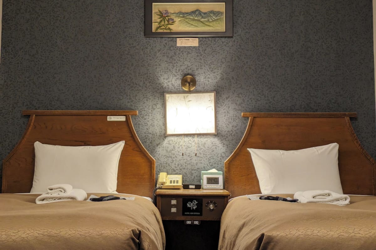 Habitación de hotel con dos camas, una mesita de noche con teléfono y reloj, y un cuadro en la pared.