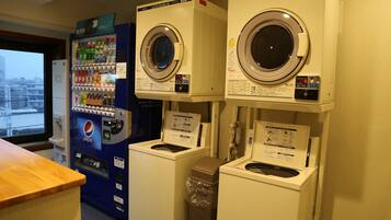 Uma área de lavanderia com duas máquinas de lavar frontais e uma máquina de vendas automática.