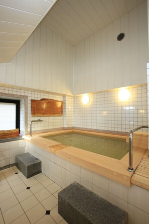 Un baño moderno con una bañera de madera, paredes con azulejos y una ventana pequeña.