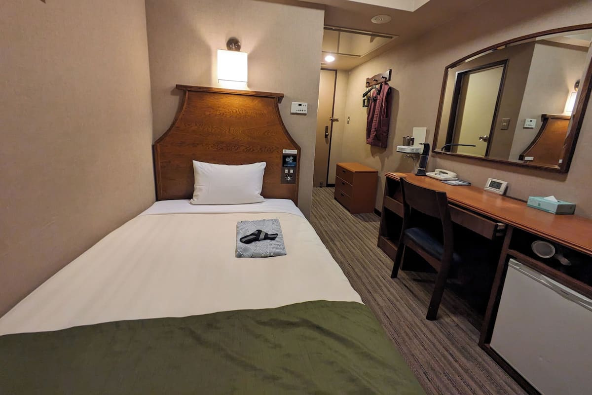Una habitación de hotel con cama, escritorio, espejo y baño pequeño.