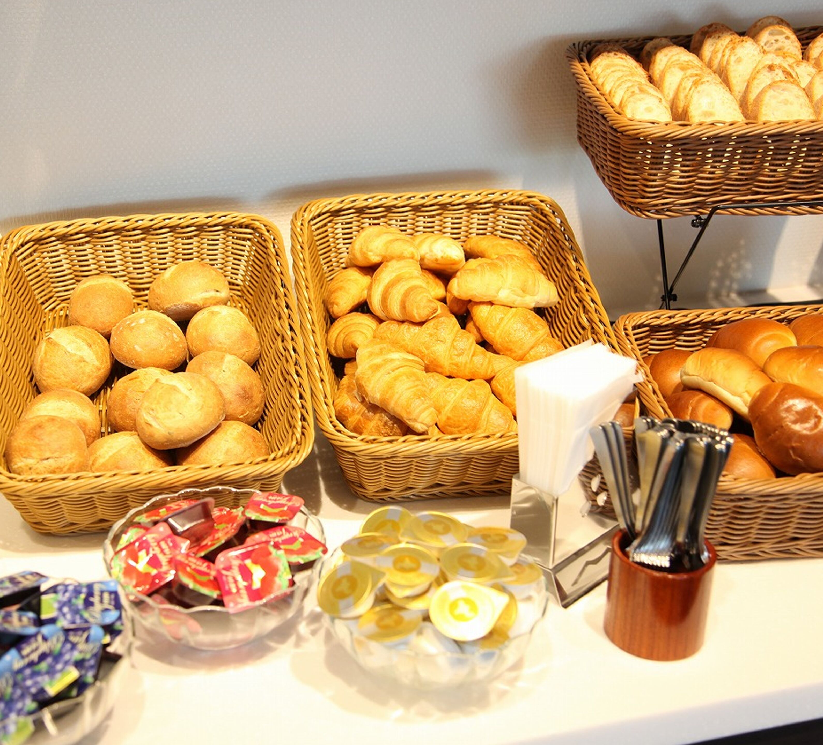 A buffet with various baked goods, including bread rolls and croissants, arranged in wicker baskets.