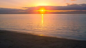 Um pôr do sol sobre águas calmas, com uma praia ao primeiro plano.