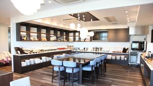 Um restaurante moderno com uma mesa comunitária grande, banquetas de bar e um balcão com diversos alimentos.