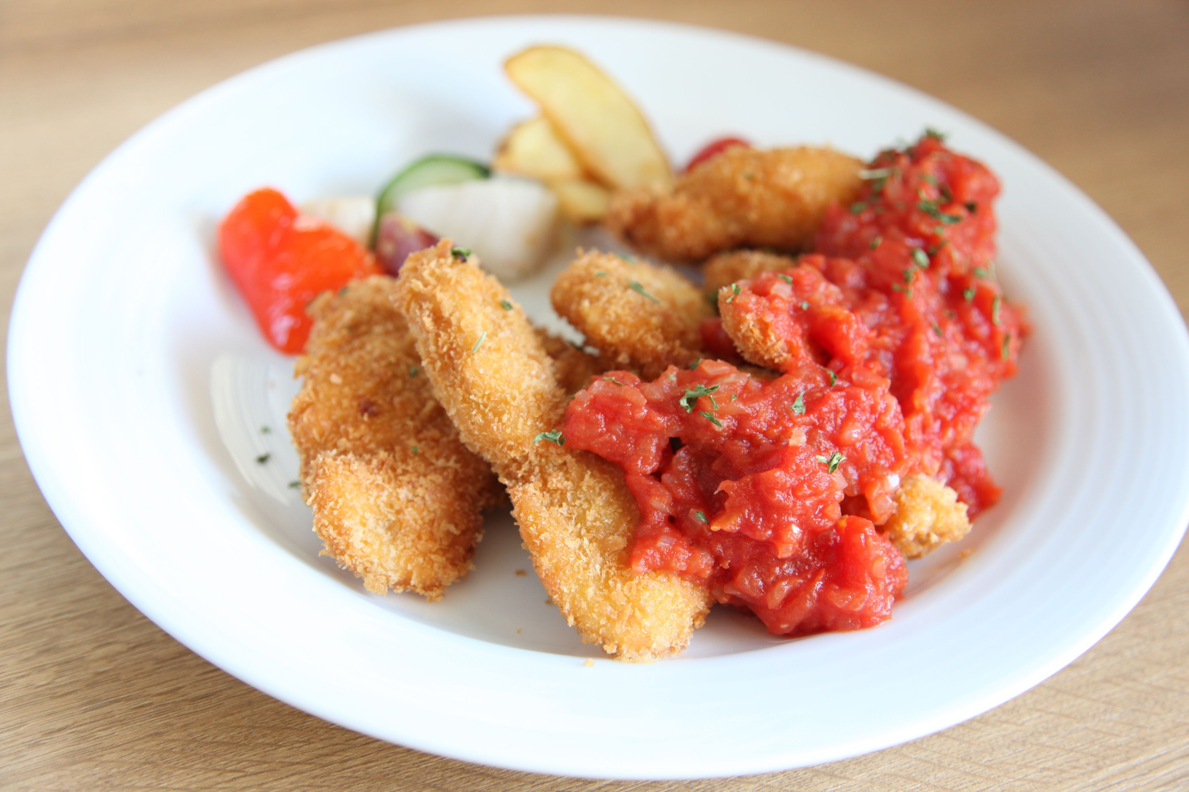 A plate with breaded and fried items, a red sauce, and some vegetables.