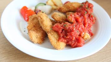 A plate with breaded and fried items, a red sauce, and some vegetables.