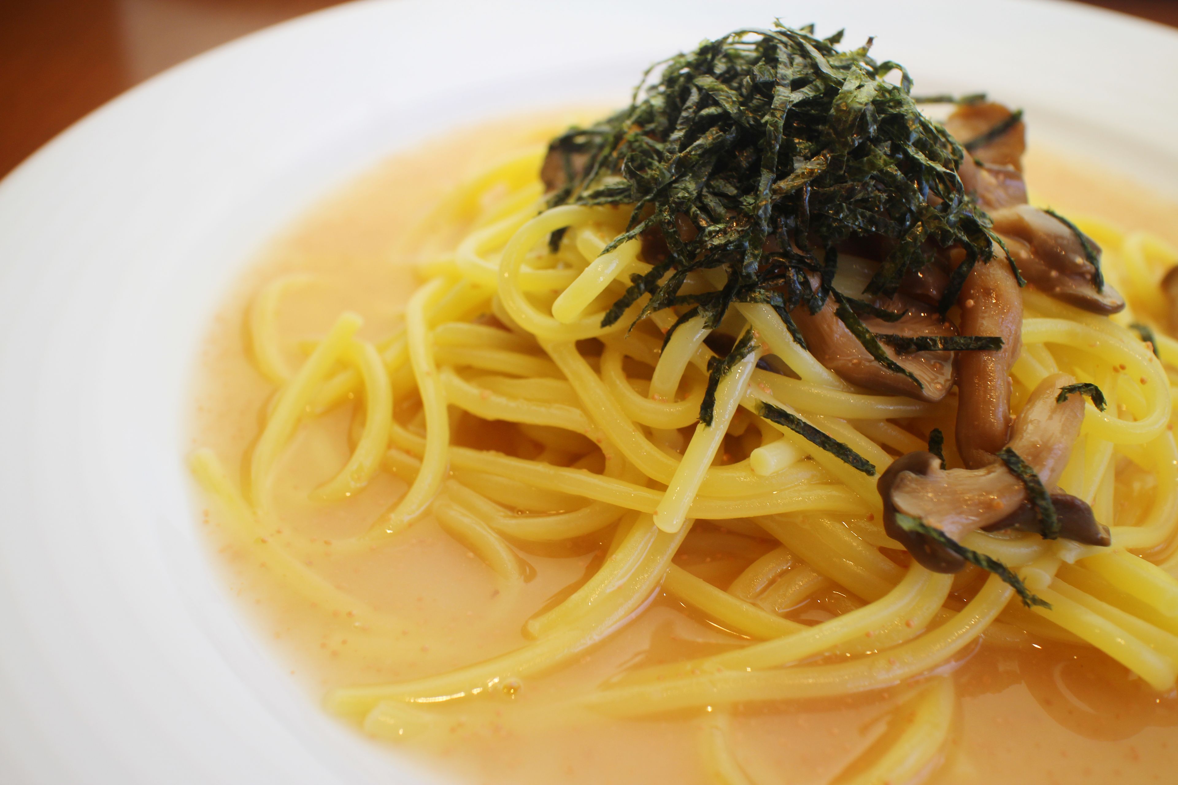 A plate of spaghetti with a creamy sauce and topped with mushrooms and seaweed.