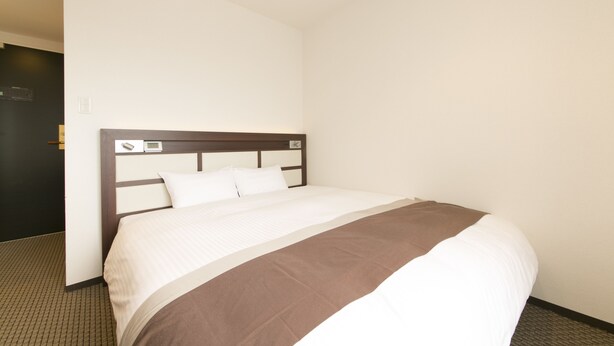 Une chambre d’hôtel avec un grand lit, une tête de lit en bois et une porte située sur le côté gauche.